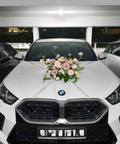 A white BMW X2 SUV parked in a garage, decorated with a pink and white floral arrangement on the hood. The car features the distinctive BMW kidney grille and LED headlights.