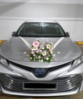 A silver Toyota sedan parked indoors, decorated with a pink and white floral arrangement on the hood and a white ribbon bow. The front license plate reads SJF 9811S.