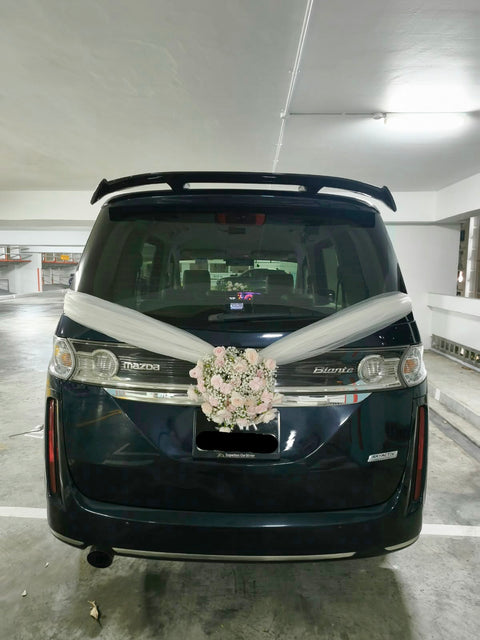 White floral wedding car arrangement with ivory ribbons on a dark van