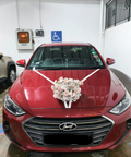 White floral bridal car bonnet arrangement with white ribbons on a red car