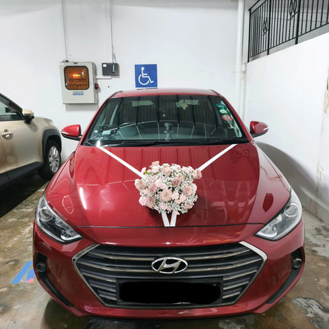 White floral bridal car bonnet arrangement with white ribbons on a red car