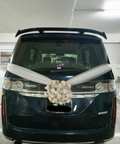 White floral wedding car arrangement with ivory ribbons on a dark van