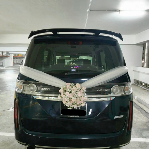 White floral wedding car arrangement with ivory ribbons on a dark van